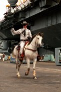 A man dressed as the Lone Ranger rides his horse along the pier as the aircraft carrier USS RANGER (CV-61) ties up behind him. The RANGER has returned to North Island following its deployment to the Persian Gulf region for Operation Desert Shield and Operation Desert Storm.